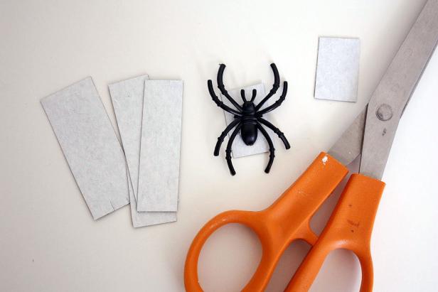 Start by cutting your magnetic strips to size: just larger than the base of the spider but smaller than the span of its legs.