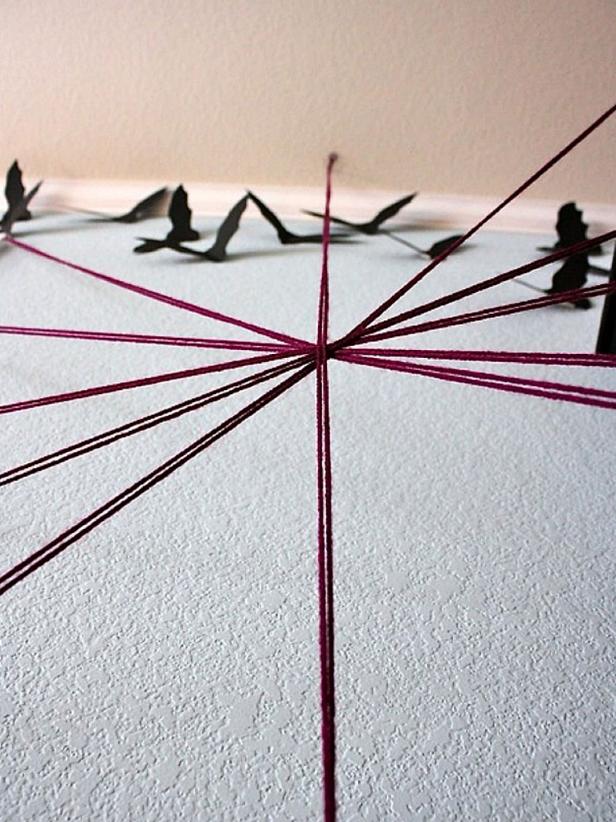 Use double strands of yarn, and tape the ends to the wall and cabinet with simple Scotch tape. Make an X, then make other crisscross lines, and finally make a big vertical strand from the ceiling down. This is so the last one could lie on the other strings and pop out (since it wasn't taped to a 3-D object like the cabinet).