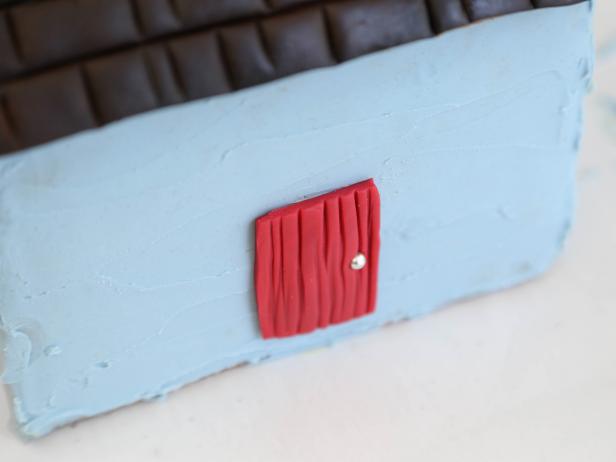 Adhere the red fondant door onto a long side of the house using a dab of royal icing.