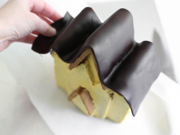 Roll out chocolate fondant and gently drape over the roof and press to adhere to the icing.