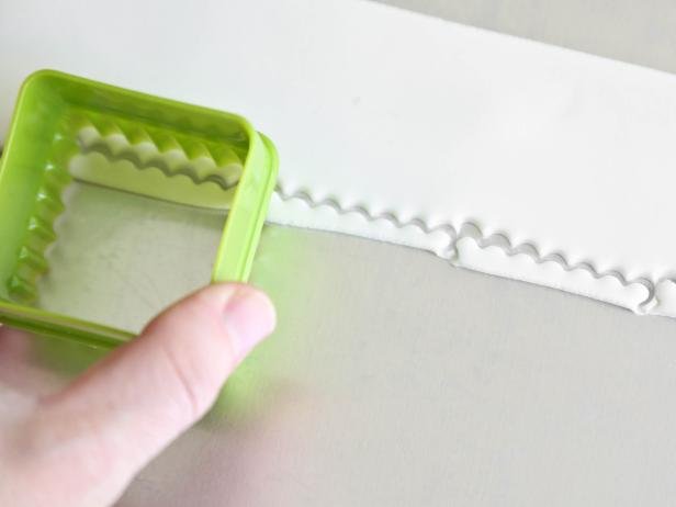 Use a cookie cutter to cut out scalloped edging from white fondant rolled to 1/4-inch thickness to create a scalloped fondant edging for a gingerbread house.