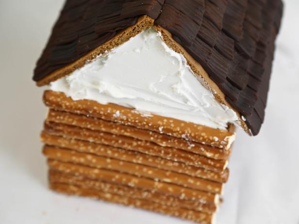 Cover front piece of the gingerbread house with royal icing using an offset spatula. Press cut pretzels into the royal icing. Repeat process on sides and back of the house.