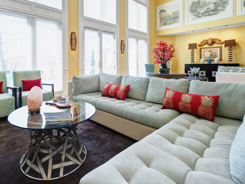 Sage Green Sectional With Red Pillows and Glass Coffee Table