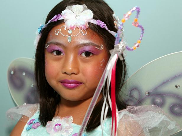 To apply fairy princess makeup, begin with a pearly eye shadow. Then add pink blush on the cheeks. Next, apply self-adhesive glittering jewels on forehead like a princess' tiara, and then apply additional jewels under eyebrows, on cheekbones or anywhere you like. Tip: You can find self-adhesive jewels in the scrapbooking section of your local craft store. Make sure your child doesn't have any adhesive allergies before continuing with this step. Keeping away from the sensitive eye area, dab face lotion on the cheeks and surrounding the jewel tiara on forehead. Have model close her eyes then apply cosmetic glitter where lotion was applied. Paint lips with a sparkly pink lipstick or tinted lip-gloss. Finish the look with a fairy princess costume.
