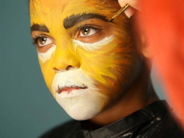 To give your child a ferocious lion’s face for Halloween, simply paint a basic orange and yellow face. Darken and thicken eyebrows with black or dark brown paint or shadow. Dip a thin paintbrush into water then coat with a generous amount of black paint. Paint nose black, focusing on the bottom tip. Next, paint a line connecting the bottom of the nose to the top lip, creating a cat-like mouth separation.