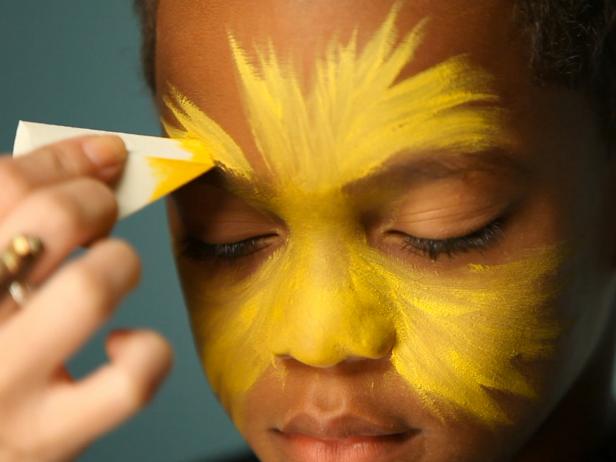 To create a base for your lion makeup, begin by dampening a sponge then picking up some of the yellow face paint. Tip: When using dry face paints, be sure to get sponge or brush wet before dipping into paint. Have child close their eyes, then apply yellow paint to the center of their face and blend out.