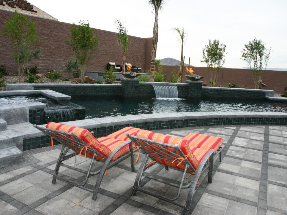 Gray Patio With Curved Pool and Bright Striped Lounge Chairs 