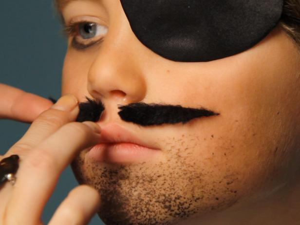 To create pirate makeup, darken the child’s eyebrows with eye shadow. Add an eye patch to one eye, and add brown shadow under the uncovered eye to mimic dark circles. Dip a stippling sponge in wet brown eye shadow or face paint, and then dab onto the chin and above the lip to give your pirate an unshaven look. Another option is to leave the top lip bare of makeup and adhere a fake mustache using eyelash glue, spirit gum or liquid latex. Tip: Be sure to test for any allergies before using any of these products, and have the proper remover on hand. Also, be sure to read all the information on product labels. Put together a costume of ripped clothing and add accessories like a bandana, a pirate hat, gold coins, a clip-on earring, hook or stuffed parrot — let your creativity run wild to give your pirate a unique look.