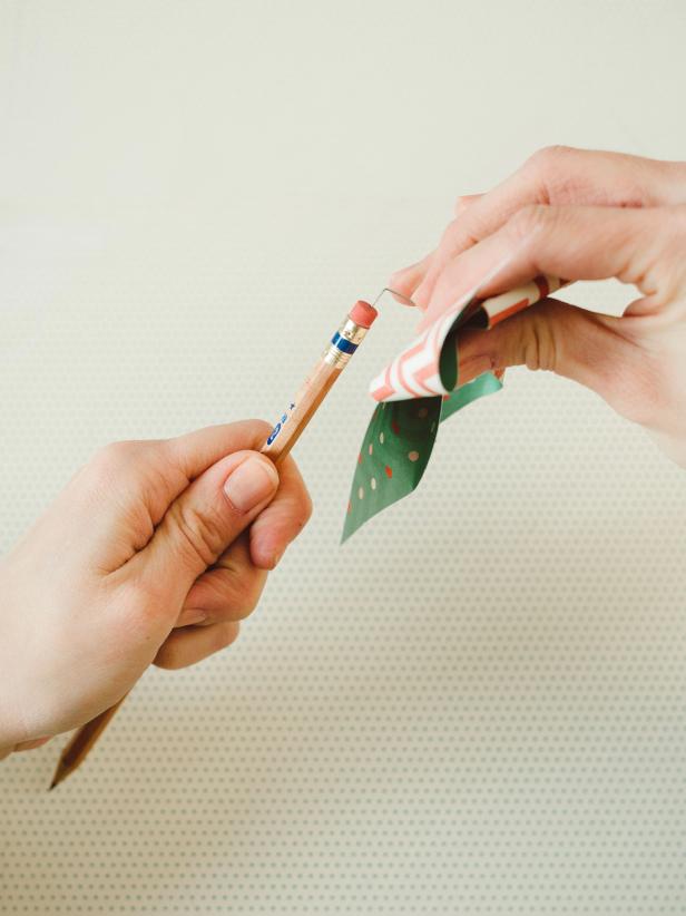 Hold the folded points in place while you push a pin through the center, being careful to catch all four folded corners. Next, gently guide paper around the bend in pin, sliding the pinwheel out to the pin's pearl end. Finally, firmly press the pin's pointed end straight down into the pencil's eraser.