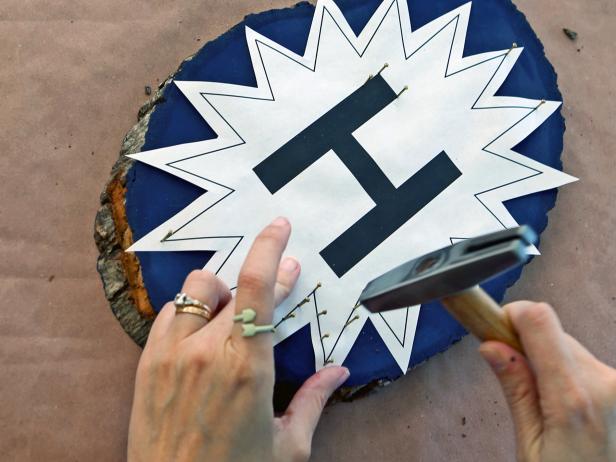 Center template onto plaque. Keep paper taut and start hammering nails into alternating points of the starburst. Continue adding nails approximately half an inch apart all around the outer edges of the starburst and letter.