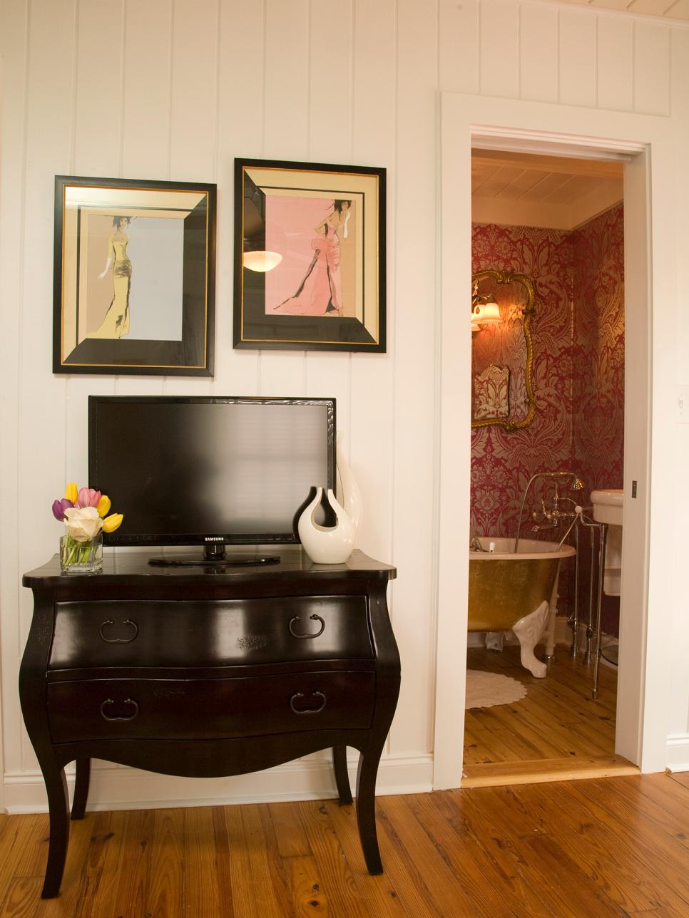 Feminine Bathroom Entrance Black Dresser and Framed Prints on White Paneled Wall Outside Bathroom