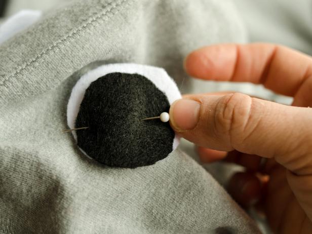 Cut out two white circles, slightly larger than the black circles. Layer felt cut-outs, black on top of white and slightly off center, to create two eyes. Pin one on each side of hood.