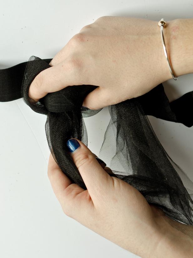 Step 3B in making a tutu as part of a child's witch costume is attaching tulle to an elastic band. After you have created a loop of tulle, wrap it around an elastic band and pull the ends through loop's center. This action will attach the tulle strips to the elastic band. Repeat with the remaining strips sliding them close together until the entire elastic band is covered.