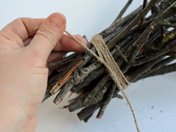 After trimming a 2-foot length of twine with scissors, Step 7D in creating a witch's broom is to wrap the twine tightly around the bunched twigs to secure them to the base of the larger stick. Add a few dabs of hot glue to any loose sticks, if necessary. Tip: This broom is a costume prop and should not be used as a toy.