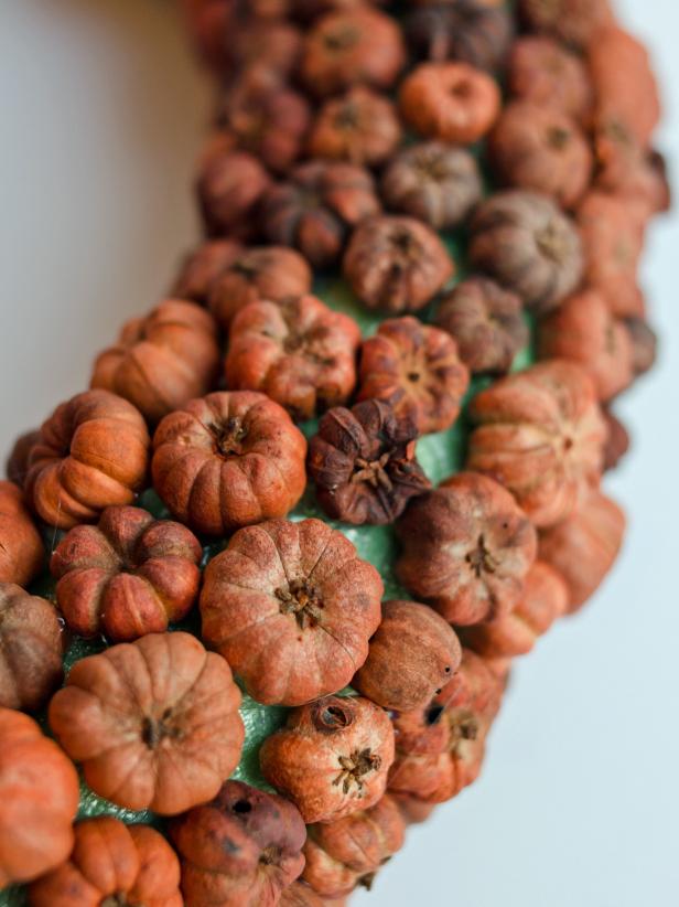 Preheat hot glue gun. Apply a small dab of hot glue to foam wreath. Immediately press a dried putka pod into hot glue and hold into place until glue cools. Repeat until entire front and sides of wreath are covered, arranging pods as close together as possible.