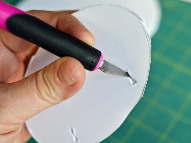 After cutting the ribbon piece in half, Step 2B is to punch four holes into one of the smaller foam core ovals using a craft knife. The holes should be in the shape of a square. The ribbon can then be threaded through the cut-outs