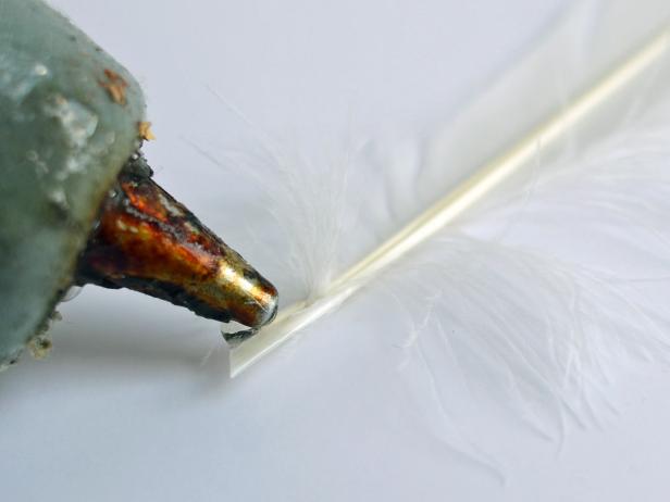 After cutting slits in the foam core board and the feather ends to size, Step 4D in making feathered angel wings is to apply a dab of hot glue to a feather's end. Insert the feather into the cut slit.