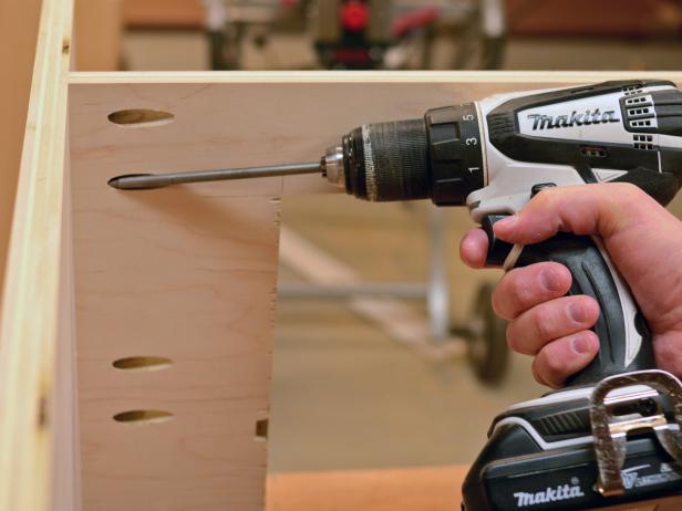 During the process of assembling a custom range hood, drill pocket holes into the bottom piece and attach it to the side panels with screws according to plan. Make sure the wood is well sanded for assembly.