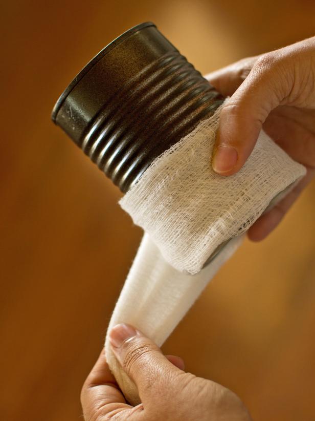 Apply hot glue to one end of the cheesecloth's length, then secure it to the tin can's back side.