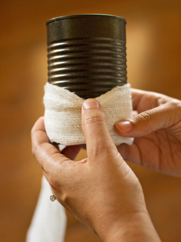Apply hot glue to one end of the cheesecloth's length, then secure it to the tin can's back side.