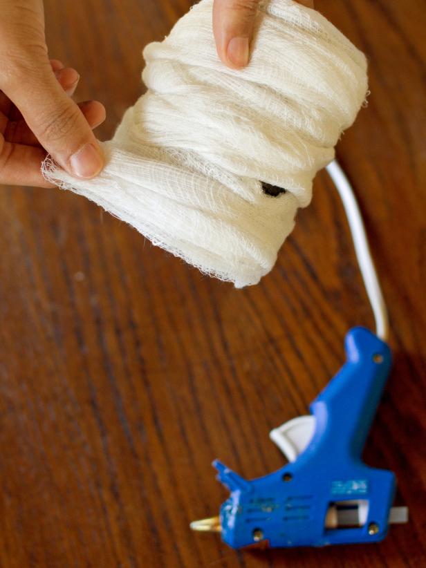 Continue wrapping the fabric all the way around the tin can from bottom to top, then back down to the bottom again. Use hot glue to secure the fabric's loose end on the can's back side.