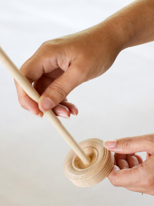 To create a mast for your ship centerpiece, use a miter saw to cut wooden dowel so it measures 4 times taller than the height of the serving container. Insert the dowel into the center hole of the wooden tread wheel.