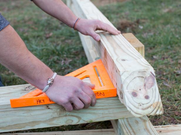 With vertical posts laid flat on ground in proper position, and with speed square in place, sandwich cross beam between each pair of 4x4s of vertical posts, tapping into place with hammer.