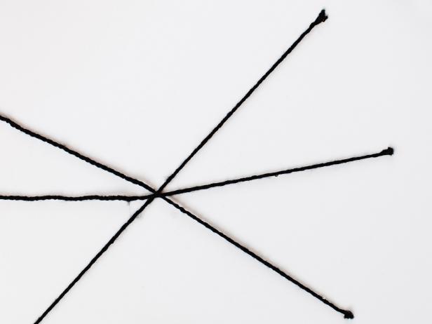 To make a spider web on the wall, begin by cutting 4 lengths of yarn about 3 feet long and attach them to the wall in a criss-cross pattern using glue dots to secure the ends.