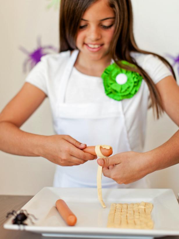 Beginning at one end of the hot dog, wrap a strip of dough around it, leaving a small gap with the hot dog showing for the eyes.