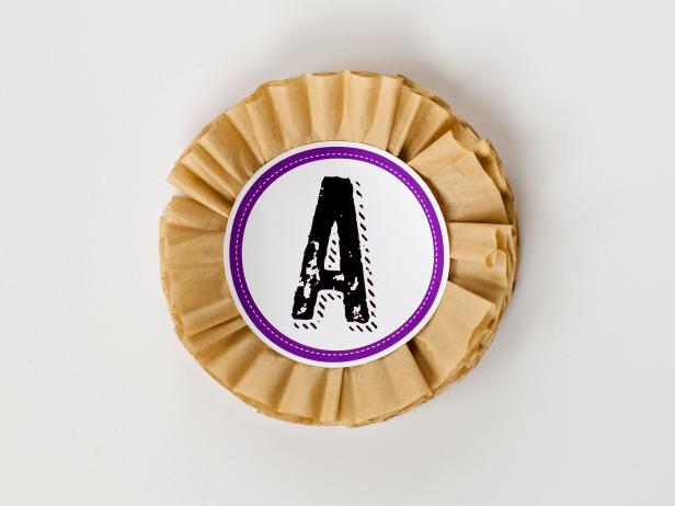 Cut out each banner panel in a circle (or use a circle cutter), with a circumference of 4 3/4 inches. Use hot glue to attach to the top of coffee filter circle.