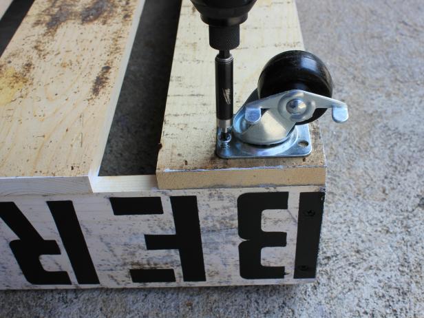 Arrange four casters along the bottom wood planks, spaced roughly three inches in from each of the four edges. Use a drill to create a hole for each, then screw them securely in place using a drill or screw gun.