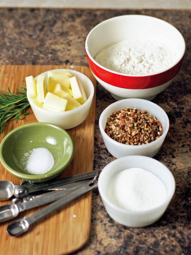 The first step is to gather ingredients for the nut crust including flour, sugar, pecans, salt, butter, egg yolk and fresh rosemary.