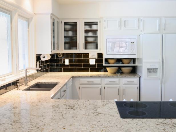 Modern Kitchen with white granite countertops and white kitchen cabinets, black tiled backsplash.