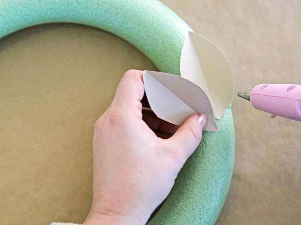 Step 4: With the hot glue gun, attach one end of the leaves to the wreath form to create the first row. Wrap the leaves to completely cover the top and sides, fanning them out from the center and alternating leaf colors.
