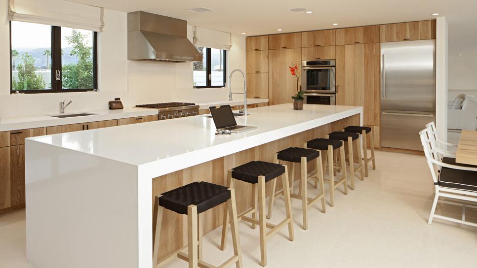 Modern Kitchen Boasts White Island With Waterfall Countertop White Modern Kitchen With White Island, Neutral Wood Cabinets & Stools