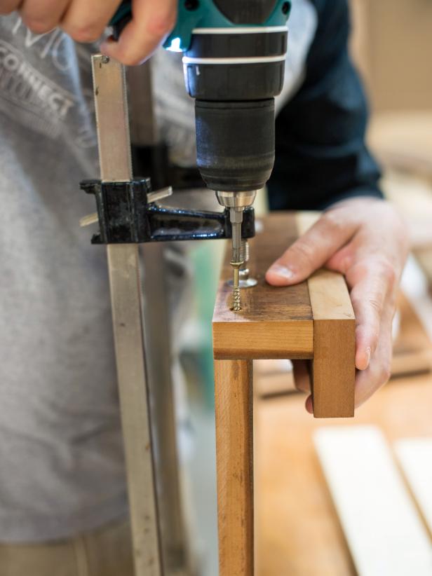 Use two bar clamps to clamp bottom piece of cookbook stand to back. Clamp to work surface as shown in picture, making sure that edges are flush. Equip drill with driver bit that matches screw heads then insert screws through pilot holes through cookbook stand back.