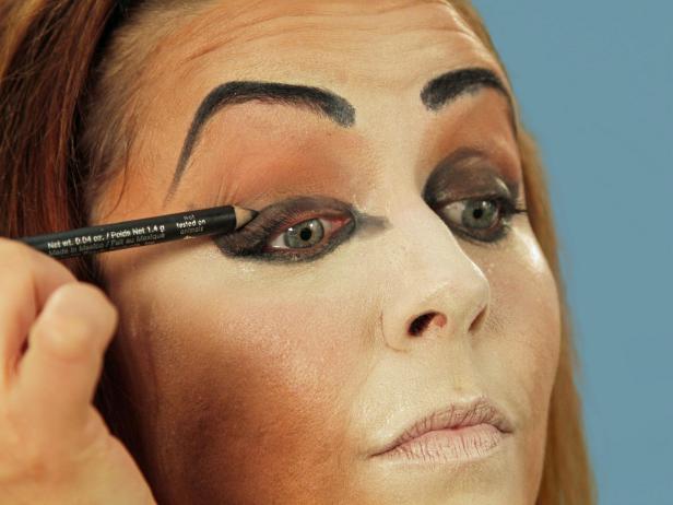 For enviable Halloween cat makeup, get the perfect base by using a makeup sponge to apply foundation that is several times lighter than your skin to the nose, middle of the forehead, under the eyes, along the cheeks and down the chin. Use a different makeup sponge and apply dark orange-brown foundation to all the areas not covered by the light foundation. Use a third sponge and lightly blend where the two colors meet. Use black eyeliner to fill in the brows. Add sharper angles over the middle of the eyes to create a dramatic peak. Heavily line the bottom lash line and extend the line out past the eye. Inside, extend the line a little down the inside of the nose. Line the top lash line and on the inside corner of the eye. Extend the top line to meet the bottom line. With the pencil, cover the eyelid, extending out beyond the eye. Blend the lines with a small, flat makeup brush to make them smooth.