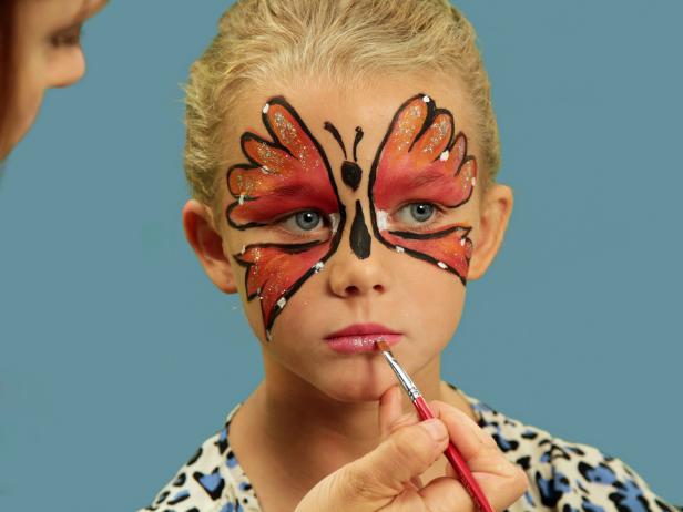 To transform your child or yourself into a beautiful butterfly for Halloween, create one large wing over each eyelid and up the forehead using face paint and a wide brush. Line wings with black eyeliner and use white face paint to add dots to wings. Create the butterfly's body between the wings by first drawing an oval above the nose with a black eyeliner pencil. From the bottom of the oval, draw a long, skinny teardrop shape to the tip of the nose to create the butterfly's body. Above the oval, draw lines onto the forehead that curl slightly at the top to resemble antennae. Finish the look with sparkly pink lips. First apply pink lipstick, and then add a dot of glitter right in the center of the lips for shimmer. A black leotard, tights and wings are all you need to complete your costume.
