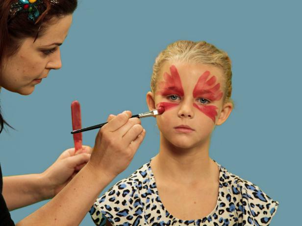 To transform your child or yourself into a beautiful butterfly for Halloween, use a wide brush to apply face paint over the eyelid and up the forehead in large strokes. Continue to make the wing strokes under the eye from the inner corner of the eye moving outward and downward. Next, use a small craft brush and orange paint to create highlights. Repeat this step using gold face paint to add more definition to each wing.