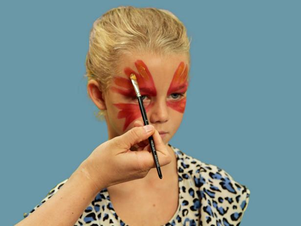 To transform your child or yourself into a beautiful butterfly for Halloween, use a wide brush to apply face paint over the eyelid and up the forehead in large strokes. Continue to make the wing strokes under the eye from the inner corner of the eye moving outward and downward. Next, use a small craft brush and orange paint to create highlights. Repeat this step using gold face paint to add more definition to each wing.
