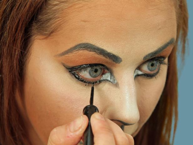 To turn yourself into an adorable cat for Halloween, cover your face with a blend of dark and light foundations to create the cat-face shape. Darken brows and create a bold cat eye with black eyeliner. Then color tip of nose black and add line from the nose to upper lip. Color top lip black. Apply a black shadow to the black areas for a more extreme cat eye. Use a white cream pencil and draw a small triangle just inside the black of the inner point. Using a large makeup brush, apply white shimmery eye shadow to the light highlights all around the face. Then, use black liquid eyeliner to accentuate the eyes by following the existing lines. Use the liner to dot on about five whisker spots above the lips on each side and draw three whiskers going out beside the nose. Add fun false eyelashes, cat ears, a tail and a collar to complete the look.