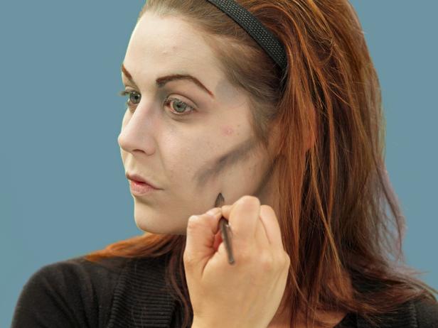 Grab a makeup brush and some gray eye shadow to add ghoulish contours to the face. Use the gray tone under the cheekbones, in the hollows of the temples, down the sides of the nose, down the jaw line, in the contours of the neck and in the crease of the eyelid and around the hollows of the eye. Use a makeup brush to add depth to these areas by blending the gray tone with black shadow in various places. To create an eerie, unnatural look, make this random and uneven on the face.