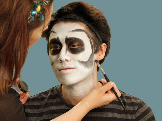 Add bony contours to skeleton makeup by using a flat craft brush to apply black cream makeup to outline the bottom of the cheekbone. Take the line close to the hairline and all the way up to the forehead, almost to the middle and about an inch over the eyebrows. Starting with the cheek, carefully use the brush to blend the line downward to create the look of a shadow. Use small moves until you get the hang of blending and, if necessary, use a makeup sponge to soften any harsh lines. Then, blend the top line down as well.