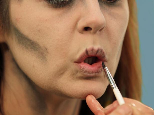 With a small, flat makeup brush, purse the lips and add black shadow to the natural lines of the lips. When the lips are relaxed they look very real for your zombie look.