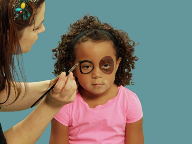 After making a filled in brown circle over one eye, switch to black paint and draw a smaller circle around the other eye. Don't fill in the black circle. The two eyes should not match.
