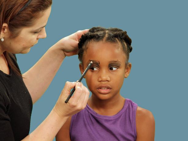 Dramatic eyes are essential for Halloween spider makeup. Using an eye shadow brush, apply dark gray eye shadow to the eyelids. Use a black eyeliner pencil to create an exaggerated brow above just one eye.