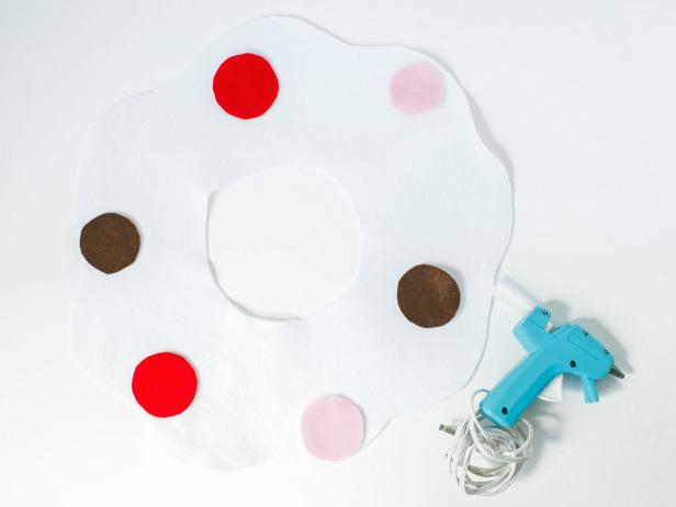 Cut two circles out of the white felt, one a bit smaller than the other. Fold each circle in half and cut out an inner circle, creating a donut. Size of circles depends on child's size. Use scissors to scallop the edges of each piece. Cut out a circles from the various felt color and hot glue them to the white frosting pieces. These will be the sprinkles.