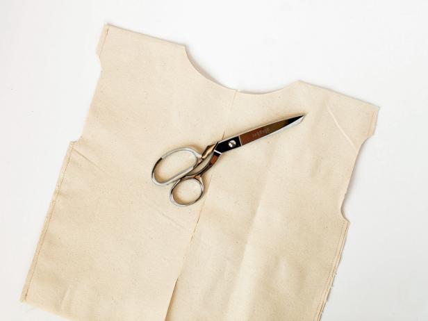 Then cut a straight line up the center of one side of the fabric toward the folded edge of fabric.Cut a small half circle where the neck will be along the folded edge of fabric.