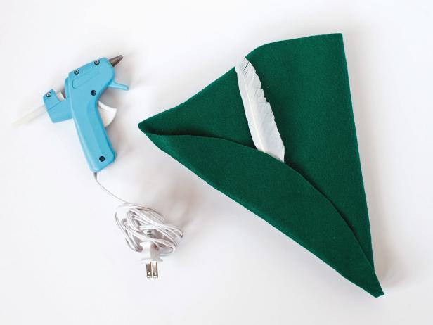 Now, you will bring the back sides around and secure the back to the size of the child’s head using a few dots of glue to secure the two edges in place.Use a dot of glue on the end of a feather to slip into the brim of the hat.