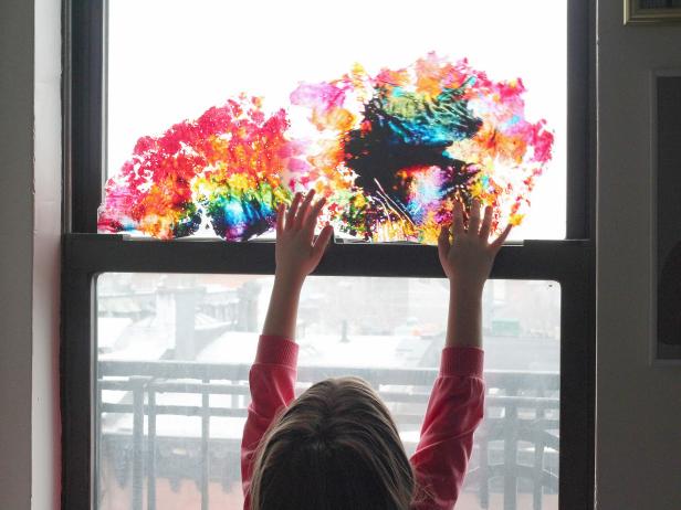 girl holding wax paper rainbow art against window